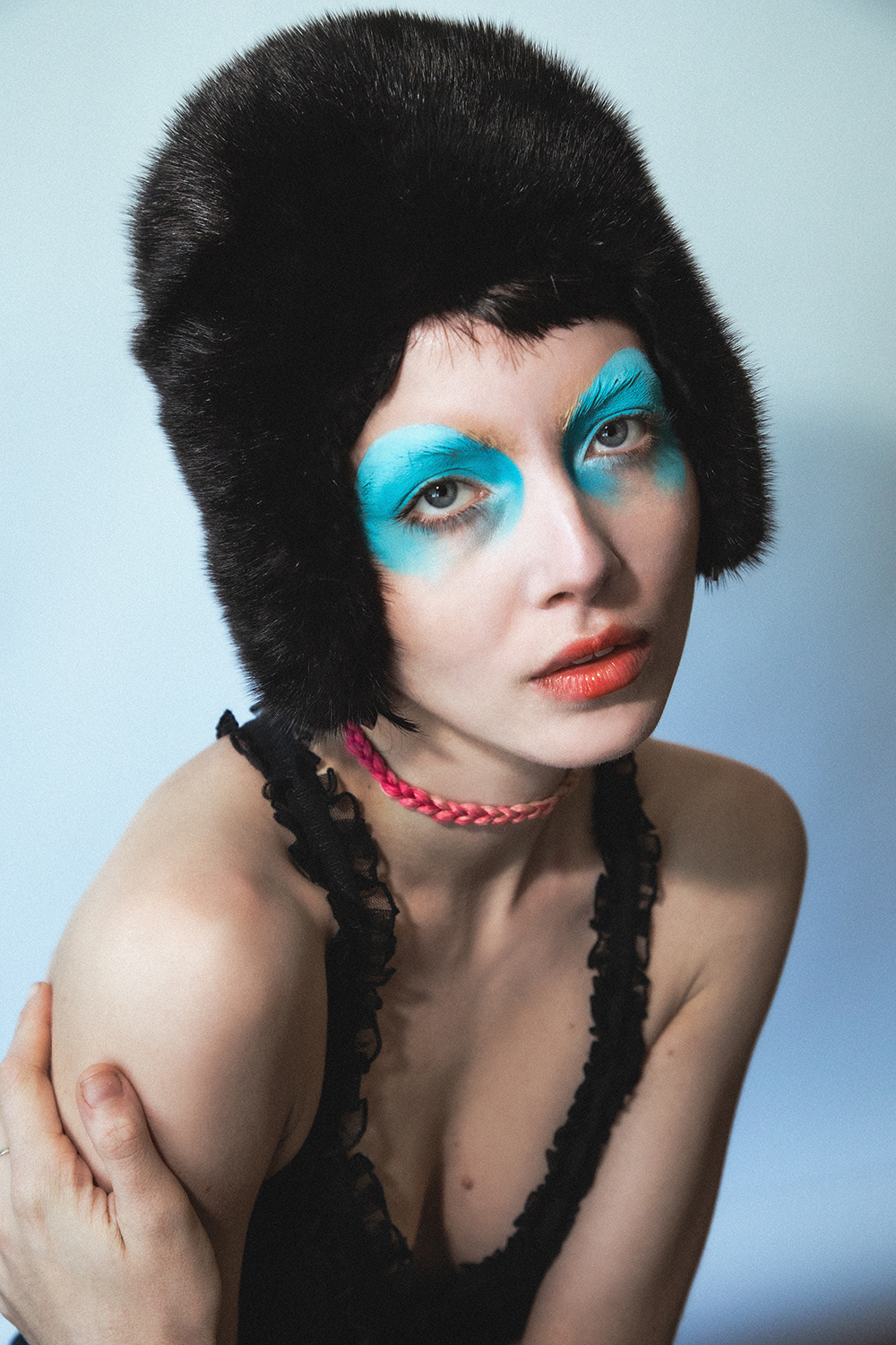 Close up portrait of Autry with bright blue graphic eye makeup in a fuzzy black hat looking at the camera